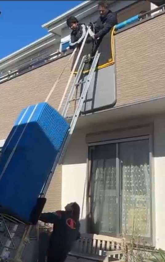 2階窓際で大型冷蔵庫を電動はしごから受け取る搬入作業