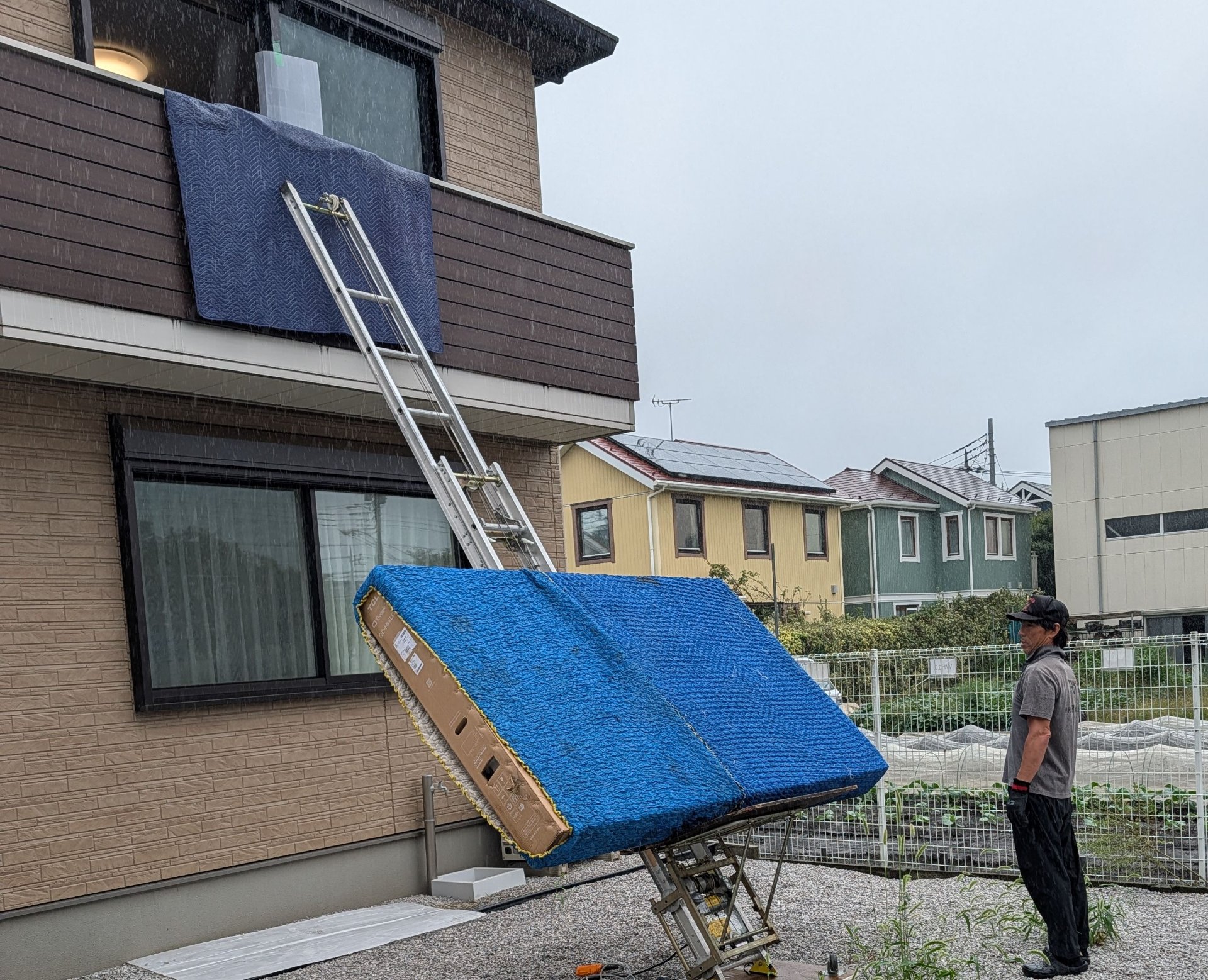 雨の中、電動はしごで2階へ大型家電を搬入する作業風景